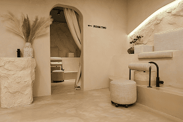 Minimalist spa interior with neutral tones, arched doorway, seating area, and soft lighting